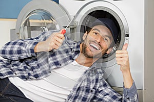 Repairman repairing washing machine giving thumbs-up