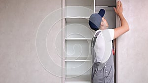 Repairman in uniform inspects broken closet in light bedroom