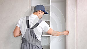 Repairman in uniform inspects broken closet in light bedroom