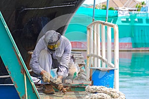 Repairman using electric steel cracker to cracking rusty stern floor of oil tanker in shipyard area at harbor