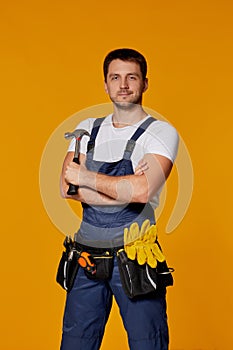 Repairman worker in yellow hard hat and uniform holding hammer.