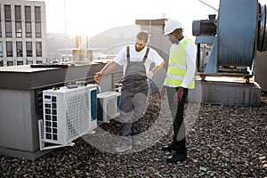 Repairmen standing and looking at conditioner on rooftop