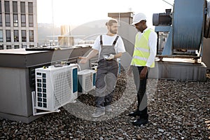 Repairmen standing and looking at conditioner on rooftop