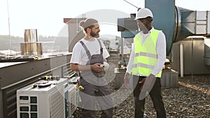 Repairmen standing and looking at conditioner on rooftop