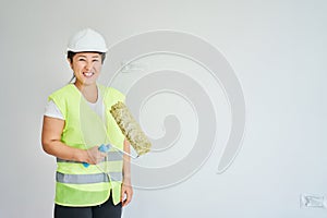 Repairs in the apartment, a girl in a green vest and a white helmet is in a white room with a roller in his hands