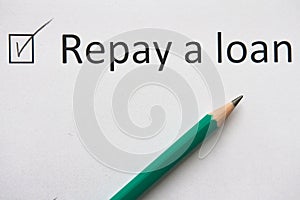 Repay a loan CREDIT. To fulfill set goal. phrase `Repay loan` is written on white paper in pencil, marked with tick.