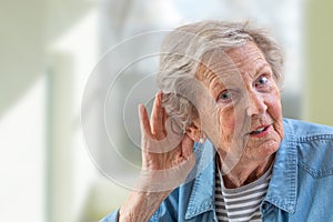 Repeat, please. Close-up of face of charming elderly woman is holding hand by her ear and struggling to hear something