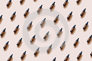 Repeating pattern from brown glass cosmetic or pharmaceutical bottles with dropper. Mockup, copy space, top view on coral