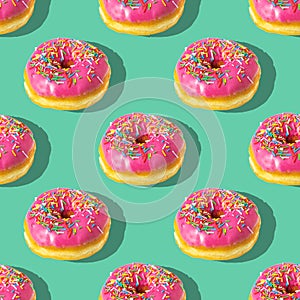 Repeating pattern of pink donuts on a green background. Flat lay