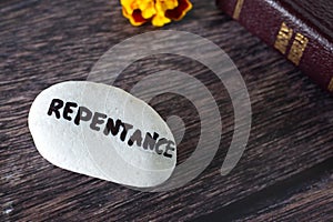 Repentance handwritten word on stone with closed holy bible book and flower on wooden background