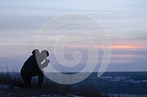 Repentance. A man on his knees. Prayer. Silhouette of a man on a blue sky background. Kneeling Prayer to God. Glorification