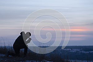 Repentance. A man on his knees. Prayer. Silhouette of a man on a blue sky background. Kneeling Prayer to God. Glorification photo
