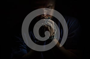 Repented man prisoner with his hands shackled in chains on a dark background