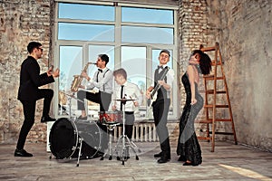 Repetition of multi ethnic jazz band in loft. Bass guitar player, electric guitar player, saxophonist and drummer at