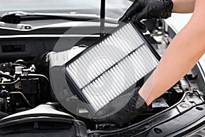Replacing the air filter in a car. Auto mechanic in gray gloves holds an engine air filter against the engine