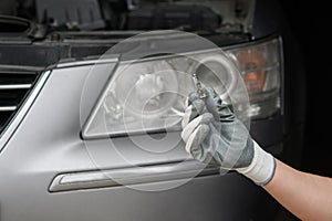 Replacing light bulbs in car headlights. Auto mechanic in gloves holding high beam halogen bulb next to car headlight.