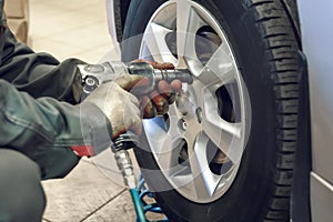 Replacing summer tires for winter using pneumatic wrench tool by mechanic worker after balancing wheels in car service garage shop