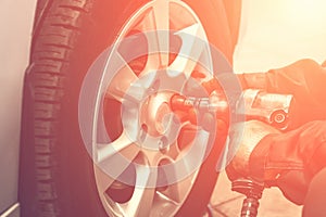 Replacing summer tires for winter using pneumatic wrench tool by mechanic worker after balancing wheels in car service garage shop