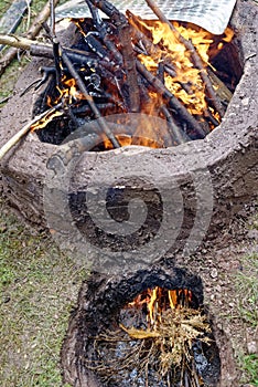 Replica of an ancient pit fire kiln with burning branches in earthen chamber