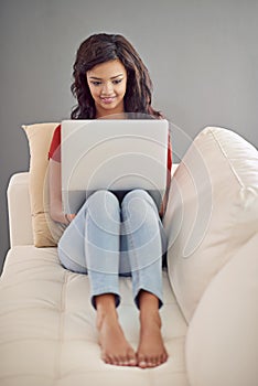 Replying to some emails. Full length shot of a young woman using her laptop while relaxing at home.