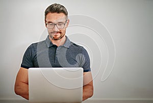 Replying to some emails. a man using his laptop while sitting against a gray wall.