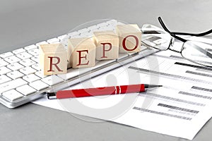 REPO Repurchase Agreement written on a wooden cube on the keyboard with chart on grey background