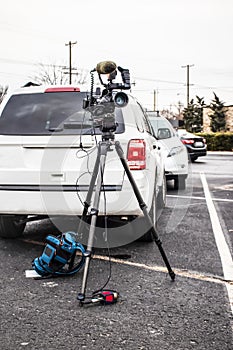 Reporters camera on tripod with backpack and microphone on ground with cars behind in a grungy parking lot - selective focus