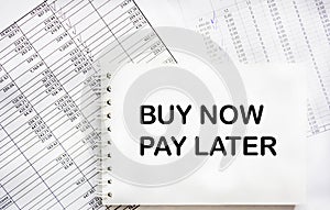 On the reports there is a notepad with the text BUY NOW, PAY LATER. Business concept