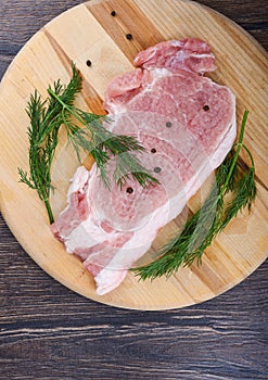 Repulsed pork steaks on a wooden cutting board with dill and spices