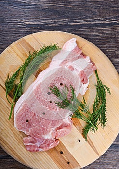 Repulsed pork steaks on a wooden cutting board with dill and spices