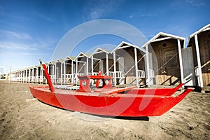 Rescue red rowing boat. Huts wooden on the beach.