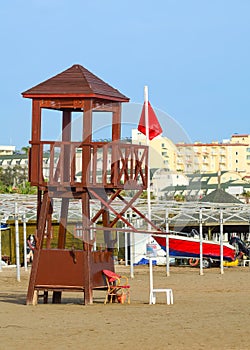 Rescue tower on an empty beach with a red flag raised. A sign prohibiting swimming in the sea.