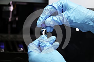 Research scientist hand with blue chemical protective gloves holding vial small bottle for doing experiment. Chemist working in