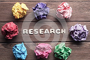 Research word and colorful crampled paper ball placed in circle on wooden table