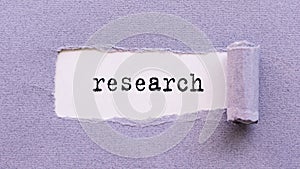 RESEARCH word written on white surface under violet torn paper