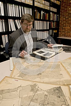 Researcher in archive, searching through maps and photographs.