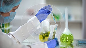 Researcher pouring blue liquid in tube with organic plant extract, analysis