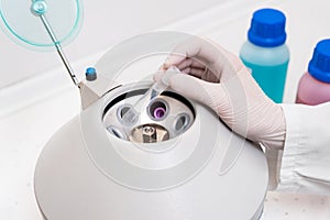 Researcher using laboratory equipment, putting sample tube in centrifuge machine to to do the lab test.