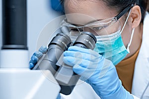 Researcher wearing safety goggles looking with the inverted microscope to look at culture cells on a slide.