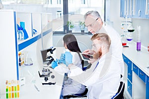 Researchers in labcoats are checking the samples on microscope i