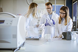 Researchers in protective workwear standing in the laboratory and analyzing liquid samples at ion chromatography equipment