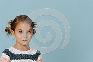 Resentful tight-lipped little girl in striped sweater, hair in buns over blue