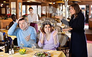 Resentful wife scolding her husband spending time with another woman at dinner