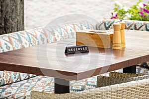 A reserved sign on a wooden table in an outdoor cafe, against a background of cutlery, wood, bushes, flowers, upholstered and