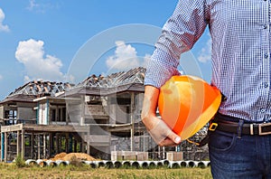 Resident engineer holding yellow safety helmet at new home building