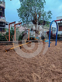 In the residential area, amidst the green trees and under a cloudy sky, a deserted playground