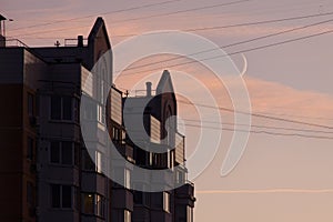 The residential building reflects in the tile and glass a beautiful sunset sky against the backdrop of a growing moon.