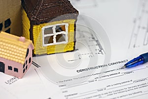 Residential construction agreement ready to sign with small toy houses and pen. Construction contract