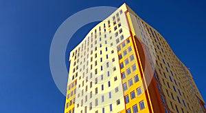 Residential high-rise building with many glass windows standing against background of blue sky and sun. Urban real