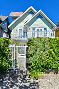 Residential house with entrance gate and green hedge in front.